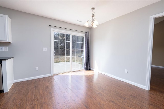 unfurnished dining area featuring dark wood-style floors, visible vents, baseboards, and an inviting chandelier