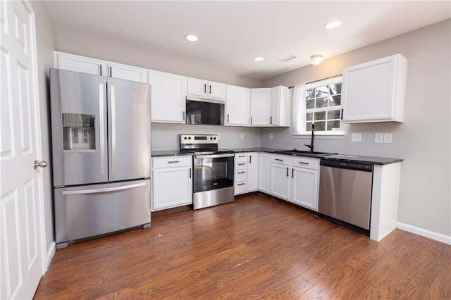 kitchen with dark wood-style floors, stainless steel appliances, dark countertops, and white cabinets