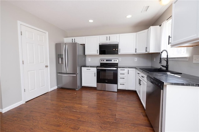 kitchen with dark wood finished floors, dark countertops, appliances with stainless steel finishes, white cabinetry, and a sink