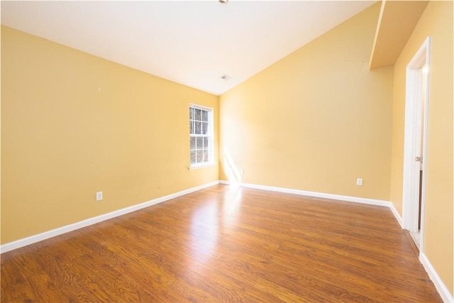 spare room with vaulted ceiling, baseboards, and wood finished floors