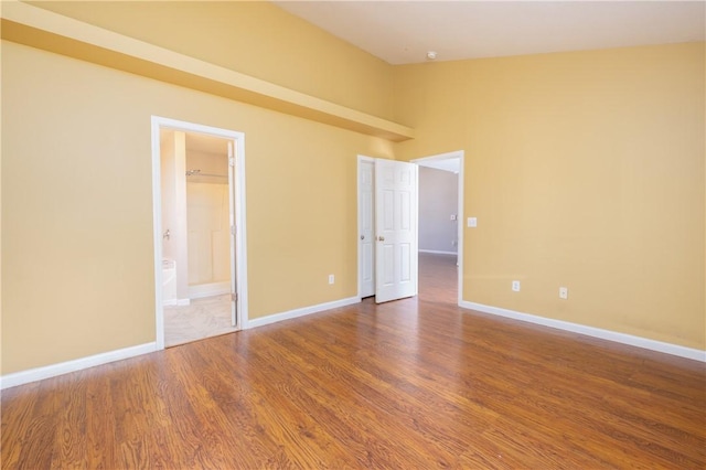 unfurnished room featuring vaulted ceiling, wood finished floors, and baseboards