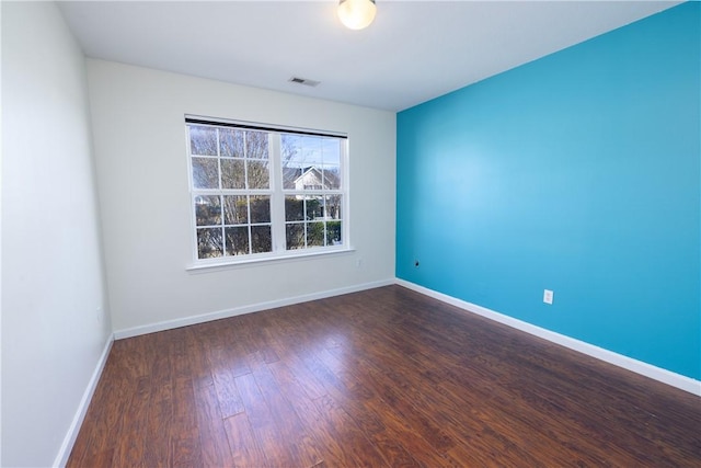 spare room featuring dark wood-style flooring, visible vents, and baseboards