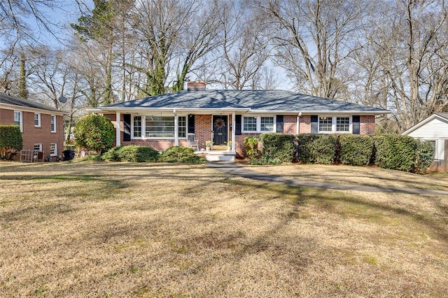 single story home featuring brick siding, a chimney, and a front yard