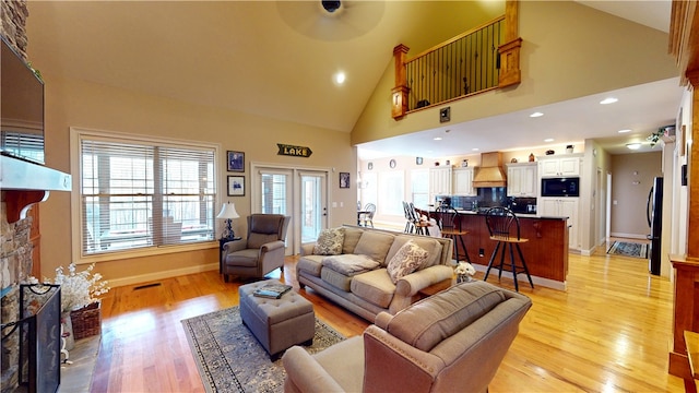 living area featuring high vaulted ceiling, a healthy amount of sunlight, a fireplace, and light wood finished floors