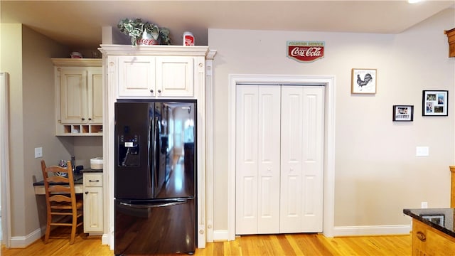 kitchen featuring dark stone counters, baseboards, black fridge with ice dispenser, and light wood finished floors