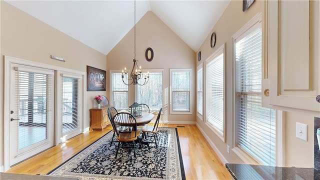 dining area with baseboards, high vaulted ceiling, light wood-type flooring, and an inviting chandelier