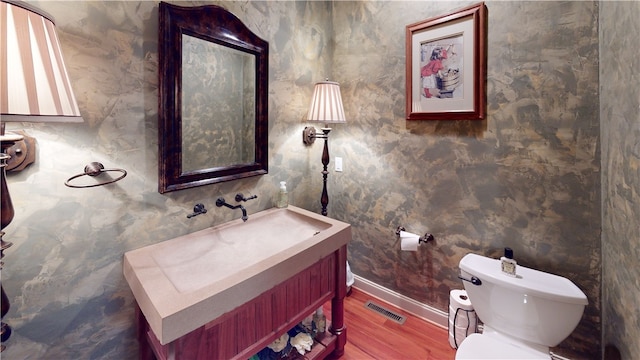 half bathroom featuring toilet, wood finished floors, vanity, visible vents, and baseboards