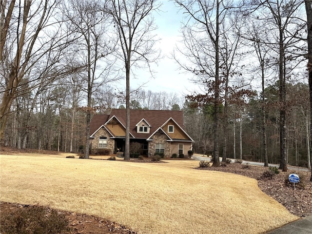 craftsman inspired home with stone siding, a view of trees, and a front yard