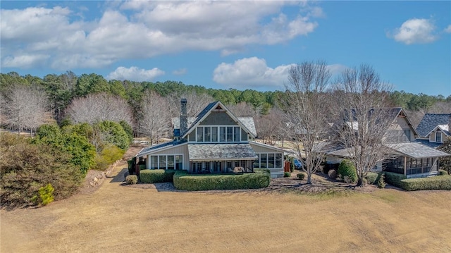 rear view of house featuring a forest view, a lawn, and a sunroom