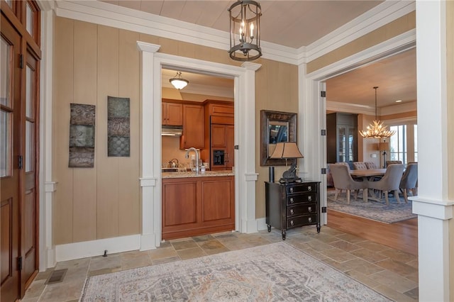 foyer featuring baseboards, visible vents, ornamental molding, stone tile flooring, and a chandelier