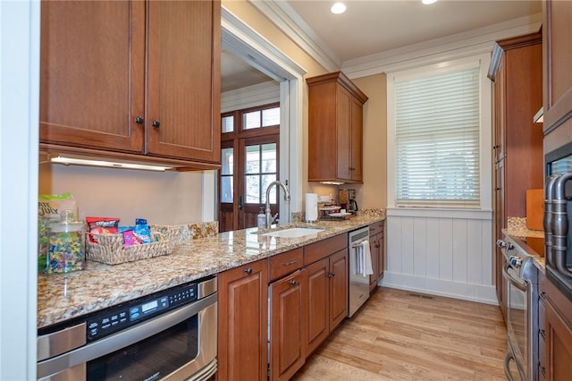 kitchen with brown cabinets, light stone countertops, stainless steel appliances, light wood-type flooring, and a sink