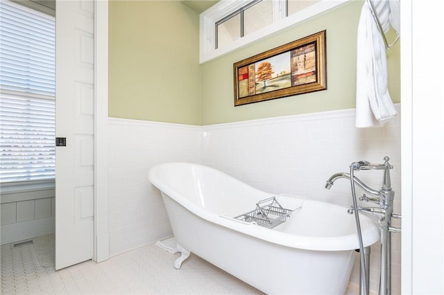 bathroom with tile patterned flooring, a wainscoted wall, a freestanding bath, and tile walls