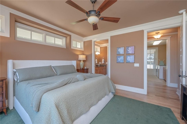 bedroom featuring ensuite bathroom, light wood-type flooring, a ceiling fan, and baseboards