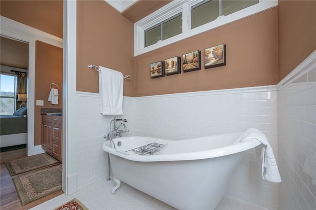 full bathroom with a wainscoted wall, a freestanding bath, tile walls, and vanity