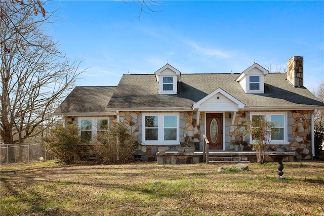 cape cod-style house featuring stone siding, a chimney, roof with shingles, crawl space, and a front lawn