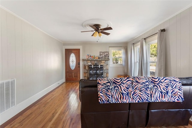 living room featuring hardwood / wood-style flooring, a ceiling fan, visible vents, baseboards, and crown molding