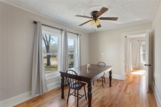 dining area featuring a textured ceiling, light wood-type flooring, a ceiling fan, and baseboards