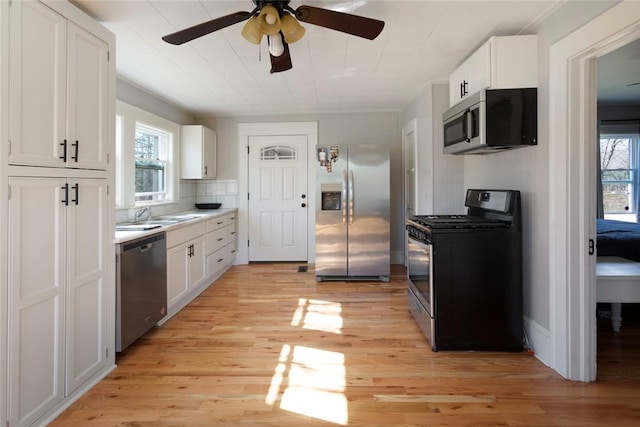 kitchen with white cabinets, appliances with stainless steel finishes, light countertops, light wood-style floors, and a sink