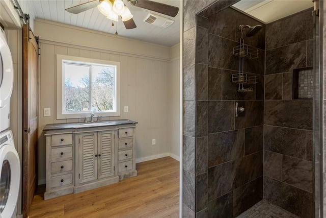 full bath with stacked washer / dryer, wood finished floors, visible vents, a ceiling fan, and a tile shower