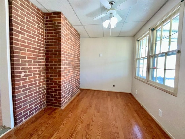 spare room with light wood-style floors, a ceiling fan, brick wall, a drop ceiling, and baseboards