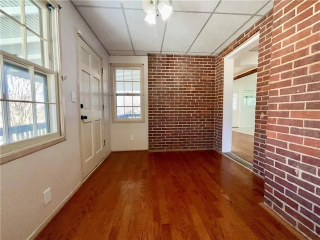 interior space featuring brick wall, wood finished floors, and a paneled ceiling