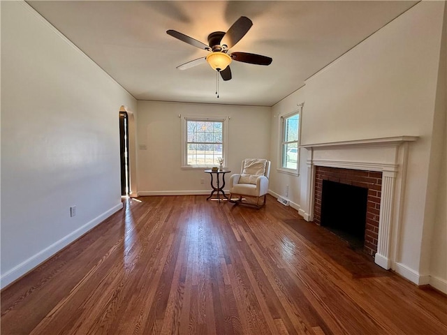 unfurnished room featuring a ceiling fan, a brick fireplace, dark wood finished floors, and baseboards