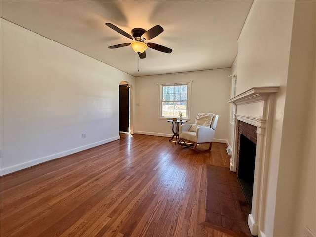 unfurnished room featuring arched walkways, baseboards, dark wood-style floors, ceiling fan, and a fireplace