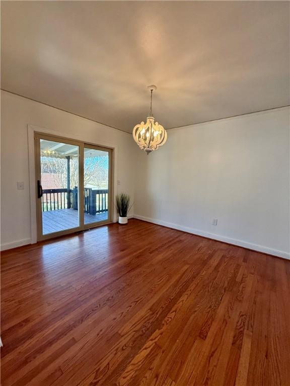 spare room featuring baseboards, wood finished floors, and a notable chandelier