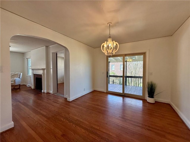 unfurnished room featuring baseboards, arched walkways, wood finished floors, an inviting chandelier, and a fireplace