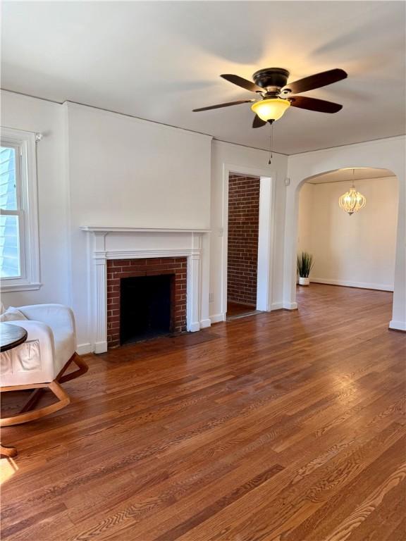 unfurnished living room featuring baseboards, arched walkways, ceiling fan, wood finished floors, and a fireplace