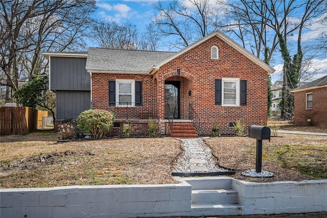 view of front of house with brick siding, fence, and roof with shingles