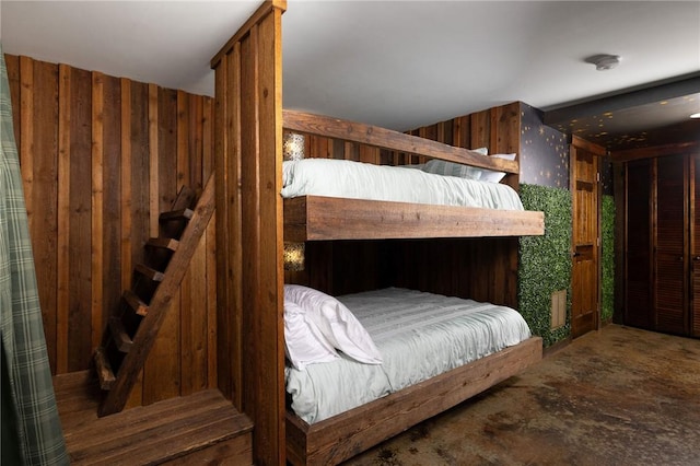 bedroom with wooden walls and unfinished concrete flooring