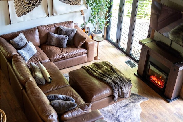 living room with visible vents, wood finished floors, and a glass covered fireplace