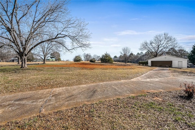 view of yard featuring a detached garage, a rural view, and an outbuilding