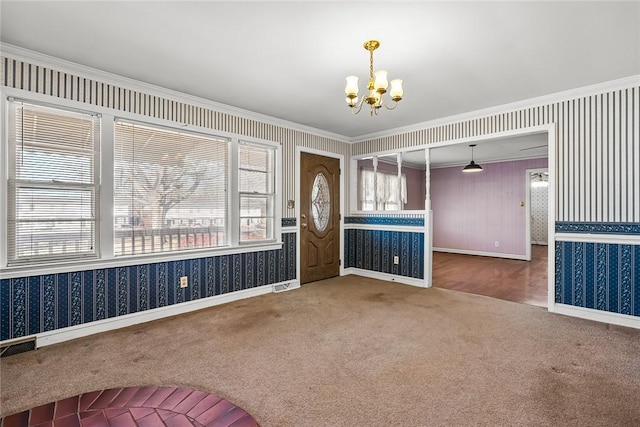 carpeted foyer with a chandelier, crown molding, and wallpapered walls