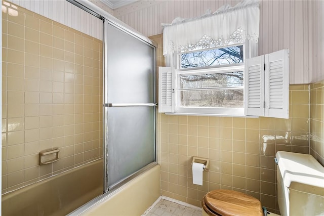 full bath featuring wallpapered walls, tile walls, toilet, and bath / shower combo with glass door