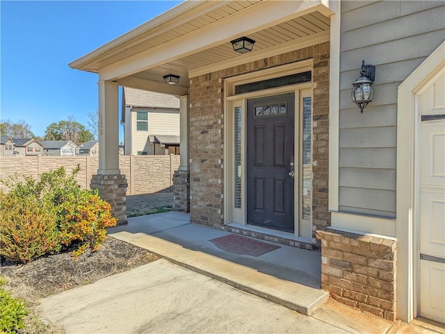 property entrance with covered porch, fence, and brick siding