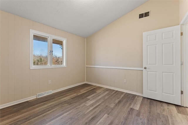 empty room featuring lofted ceiling, visible vents, a textured ceiling, and wood finished floors