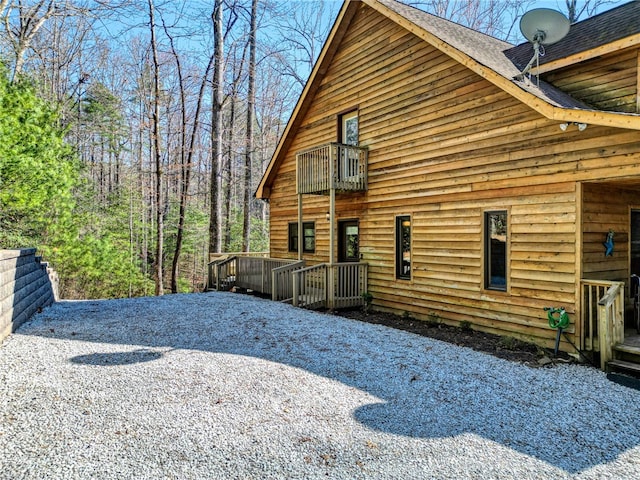 view of side of property with a balcony, driveway, and a shingled roof