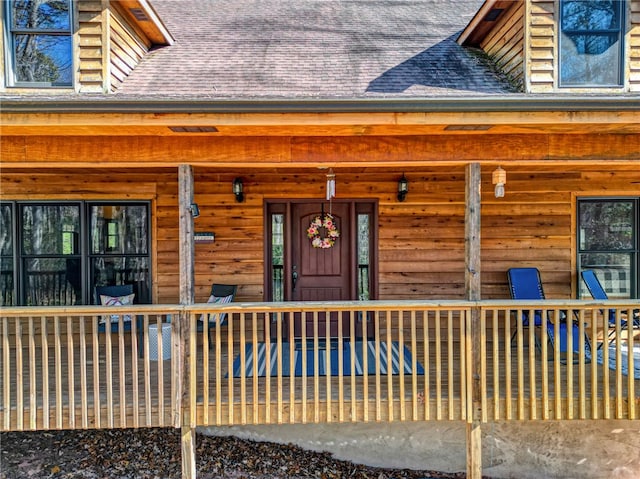 view of exterior entry featuring covered porch and a shingled roof