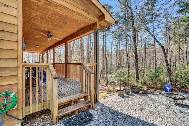 deck featuring an outdoor fire pit, a wooded view, and a ceiling fan