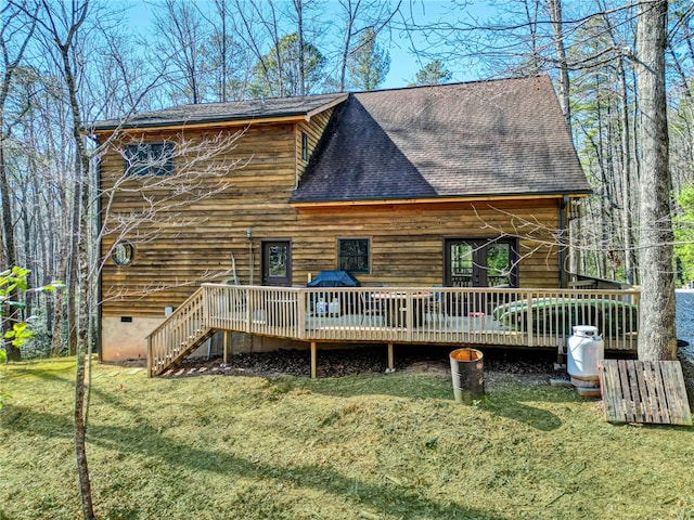 back of property with a wooden deck, a shingled roof, and a yard