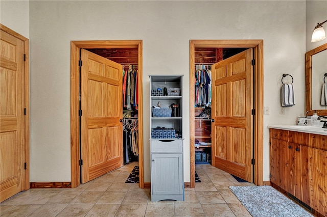 interior space featuring tile patterned flooring, baseboards, a walk in closet, and vanity