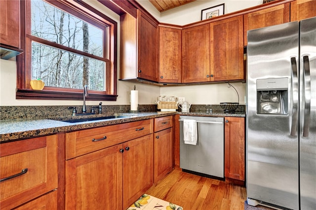 kitchen with light wood finished floors, appliances with stainless steel finishes, a sink, and brown cabinets