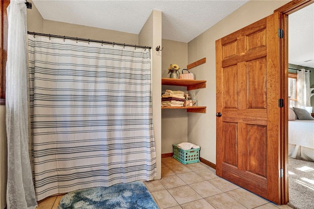 ensuite bathroom featuring connected bathroom, a textured ceiling, a shower with curtain, baseboards, and tile patterned floors