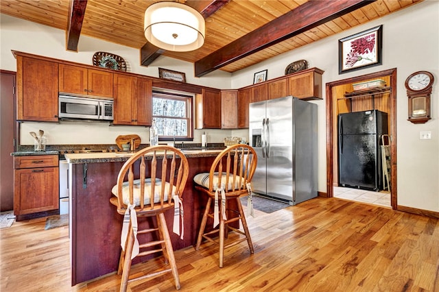 kitchen with dark countertops, wood ceiling, a breakfast bar area, stainless steel appliances, and light wood-style floors