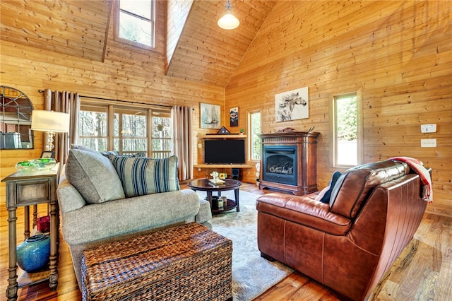 living area with high vaulted ceiling, wood walls, a fireplace, and wood finished floors