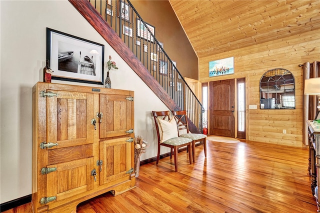 foyer featuring light wood-type flooring, stairs, wooden walls, and a towering ceiling