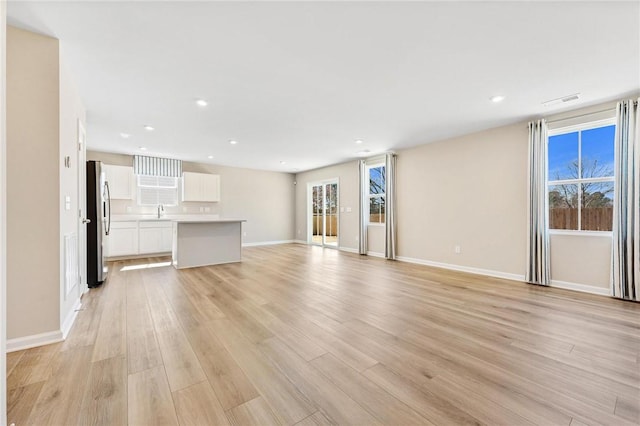 unfurnished living room with a wealth of natural light, a sink, light wood-style flooring, and recessed lighting