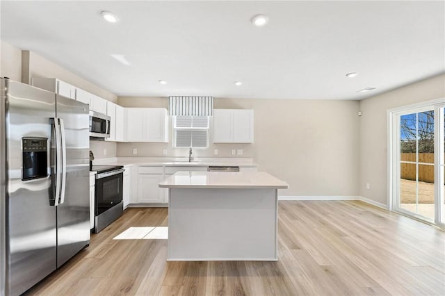 kitchen with stainless steel appliances, a kitchen island, white cabinets, light wood-style floors, and light countertops